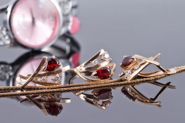 Gold earrings with rubies and elegant women's watches — Stock Photo, Image