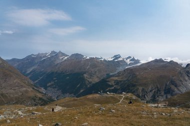 Zermatt, İsviçre - 19 Ağustos 2025: Arka planda Zermatt şehri ve teleferikli yürüyüşçüler, Matterhorn patikasındaki Alplerde yaşayan insanları taşıyorlar.