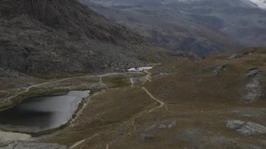 Matterhorn, ön planda İsviçre bayrağı bulunan Riffelsee Gölü 'ne yansıyarak, İsviçre' nin Zermatt kentinde alp manzarası ve turkuaz buzul suları sergiliyor..