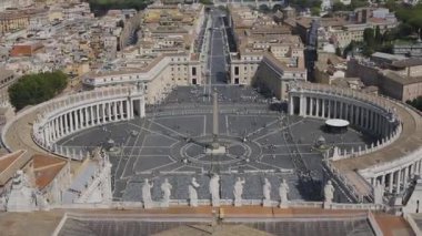Vatikan 'daki St. Peters Meydanı' nın geniş bir manzarası var. Merkezi dikili taş, kavisli sütunlar ve tarihi papalık meydanındaki ziyaretçi kalabalığı yer alıyor..