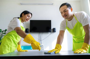 Çevre dostu ofis temizliği hizmeti sunan önlüklü profesyonel temizlikçi çift, sağlıklı bir iş yeri için pencere, bilgisayar ve toplantı odalarını sterilize ederken yeşil ürünler kullanıyor.