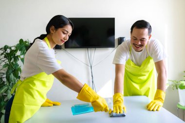 Çevre dostu ofis temizliği hizmeti sunan önlüklü profesyonel temizlikçi çift, sağlıklı bir iş yeri için pencere, bilgisayar ve toplantı odalarını sterilize ederken yeşil ürünler kullanıyor.