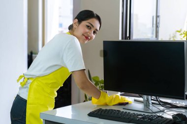 Modern ofis çalışma alanını sterilize eden profesyonel kadın temizleyici, temiz, hijyenik ve üretken bir iş ortamı sağlamak için masaları ve ekipmanları siliyor.