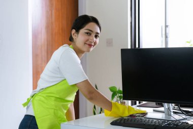 Modern ofis çalışma alanını sterilize eden profesyonel kadın temizleyici, temiz, hijyenik ve üretken bir iş ortamı sağlamak için masaları ve ekipmanları siliyor.