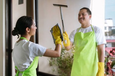 Çevre dostu ofis temizliği hizmeti sunan önlüklü profesyonel temizlikçi çift, sağlıklı bir iş yeri için pencere, bilgisayar ve toplantı odalarını sterilize ederken yeşil ürünler kullanıyor.