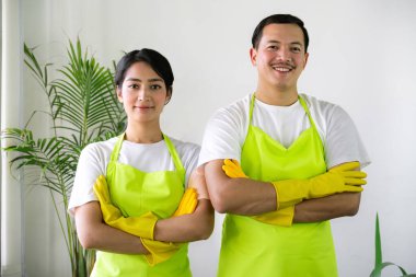 Çevre dostu ofis temizliği hizmeti sunan önlüklü profesyonel temizlikçi çift, sağlıklı bir iş yeri için pencere, bilgisayar ve toplantı odalarını sterilize ederken yeşil ürünler kullanıyor.