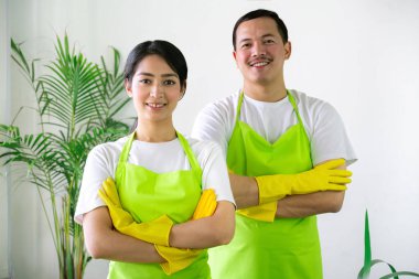 Çevre dostu ofis temizliği hizmeti sunan önlüklü profesyonel temizlikçi çift, sağlıklı bir iş yeri için pencere, bilgisayar ve toplantı odalarını sterilize ederken yeşil ürünler kullanıyor.