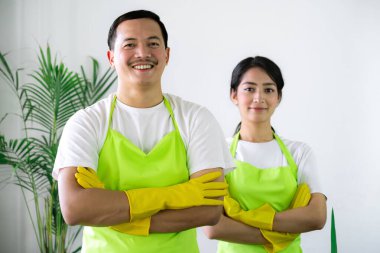 Çevre dostu ofis temizliği hizmeti sunan önlüklü profesyonel temizlikçi çift, sağlıklı bir iş yeri için pencere, bilgisayar ve toplantı odalarını sterilize ederken yeşil ürünler kullanıyor.