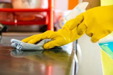 Profesyonel erkek temizleyici modern mutfağı dezenfekte ediyor, tezgah ve aletleri temizleyip hijyenik ve güvenli bir yemek ortamı sağlıyor..
