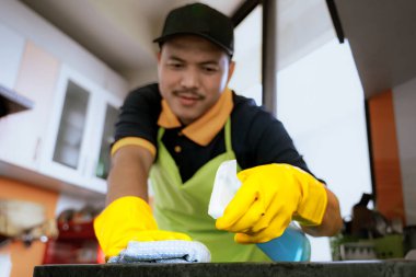 Profesyonel erkek temizleyici modern mutfağı dezenfekte ediyor, tezgah ve aletleri temizleyip hijyenik ve güvenli bir yemek ortamı sağlıyor..