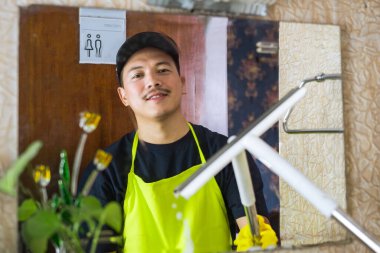 Asyalı profesyonel erkek, cam silici ve kumaşlı pencere ve aynalar, ticari ve konut alanları için çizgiden arınmış cam cilası hizmeti sunuyor..
