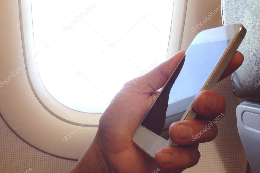 Business man sits in airplane watching his cell phone