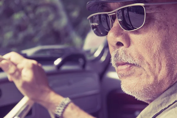 Homme plus âgé avec des lunettes conduisant une voiture — Photo