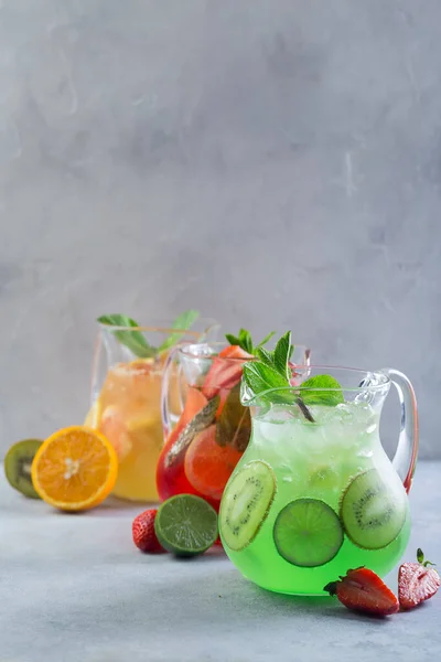 Different color lemonade in glass decanters with fruits and garnished with fresh mint and sliced fruits — Stock Photo, Image