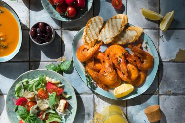 Fayans masasındaki Akdeniz yemekleri: deniz ürünleri karidesleri, sebze salatası, kabak çorbası, tohumlar