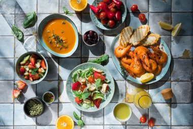 Fayans masasındaki Akdeniz yemekleri: deniz ürünleri karidesleri, sebze salatası, balkabağı çorbası, tohum ve meyve limonatası