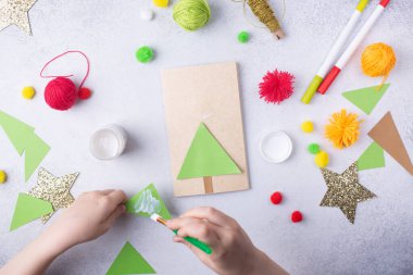 Çocuk bir tebrik kartı hazırlıyor. Noel kâğıdı kolajı. Çocuklar için sanat projeleri