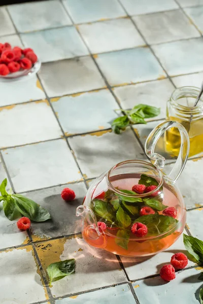 Горячий малиновый чай в прозрачном чайнике на каменном столе. Свежие ягоды, мята, стеклянная чашка — стоковое фото