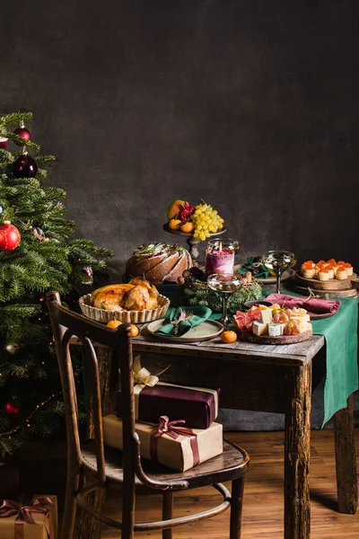 Elegante tavola apparecchiata per la cena di famiglia di Natale con albero di Natale sullo sfondo e regali sulla sedia. — Foto Stock