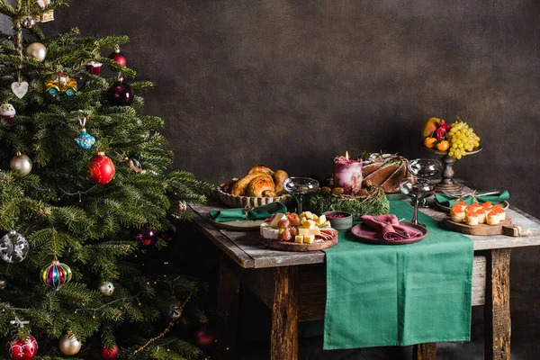 Stilvolle Tischdekoration für das Weihnachtsessen mit Weihnachtsbaum auf dem Hintergrund und Geschenken auf dem Stuhl. — Stockfoto