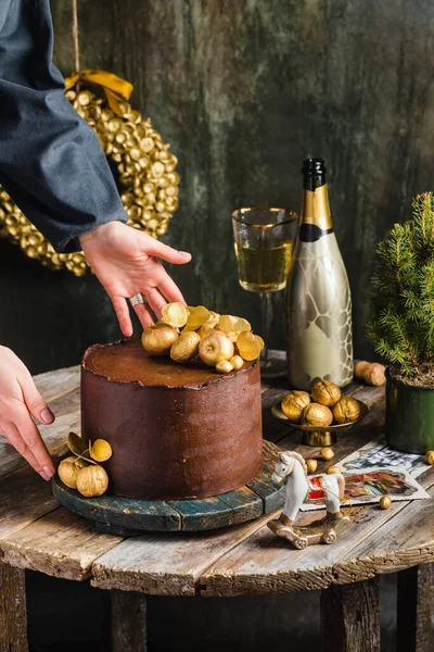 Pastel de chocolate con champán de decoración de oro detrás de manos de mujer de estilo rústico — Foto de Stock