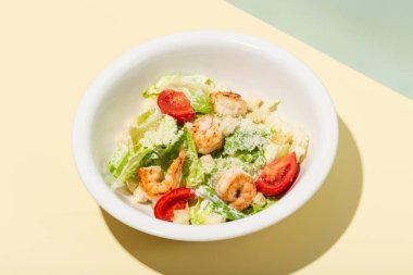 Beyaz tabakta karidesli Sezar salatası. Sarı sert gölge modern.