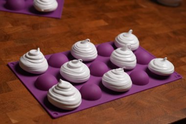 Profesyonel pasta şefi, parlak Fransız kremasını fırın tepsisine koydu. Düşük sıcaklıkta pişirmeye hazır. Klasik beyaz kremalı, mükemmel kıvrımlı, silikon hasırlar ya da fırın kağıdı üzerinde düzenli sıralanmış. Taze ev yapımı tatlı.