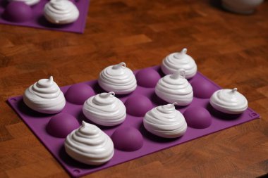 Profesyonel pasta şefi, parlak Fransız kremasını fırın tepsisine koydu. Düşük sıcaklıkta pişirmeye hazır. Klasik beyaz kremalı, mükemmel kıvrımlı, silikon hasırlar ya da fırın kağıdı üzerinde düzenli sıralanmış. Taze ev yapımı tatlı.