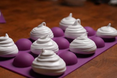 Profesyonel pasta şefi, parlak Fransız kremasını fırın tepsisine koydu. Düşük sıcaklıkta pişirmeye hazır. Klasik beyaz kremalı, mükemmel kıvrımlı, silikon hasırlar ya da fırın kağıdı üzerinde düzenli sıralanmış. Taze ev yapımı tatlı.