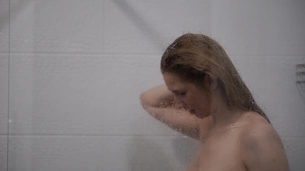 Женщина моет волосы за стеклом душевой кабинки — стоковое видео