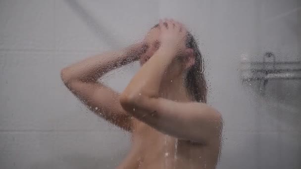 Frau wäscht Haare hinter Glas der Duschkabine — Stockvideo