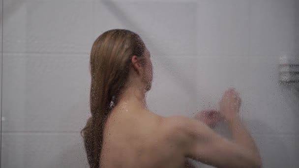 Vrouw wassen haar achter glas van douche kraam — Stockvideo