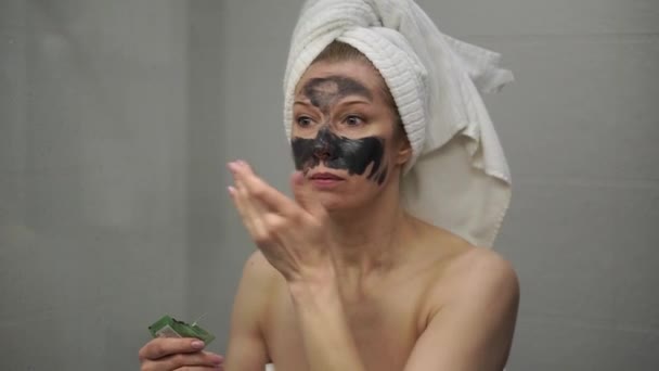 Una mujer adulta se aplica una máscara de crema en la cara — Vídeo de stock