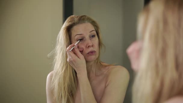 Volwassen vrouw aanbrengen van make-up in de voorkant van een spiegel — Stockvideo