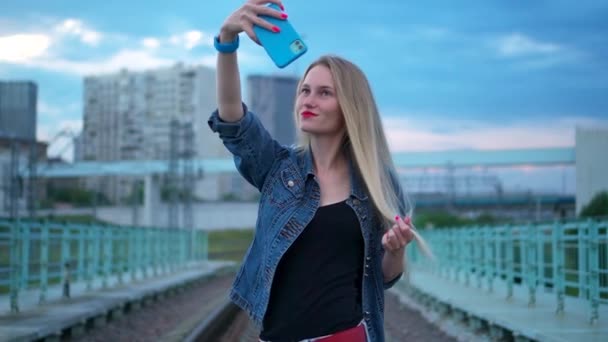 Een jonge vrouw, blond, op het spoor, neemt een selfie en een smartphone. — Stockvideo