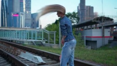 Genç sarışın kadın şehirdeki tren raylarında yürüyor.