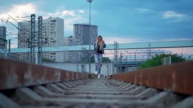 Genç sarışın kadın şehirdeki tren raylarında yürüyor.