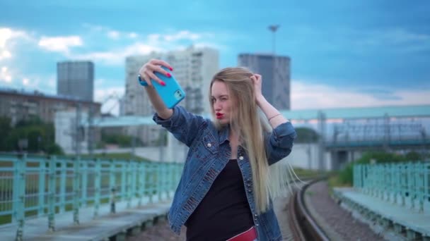 En ung blondine på skinnene tar en selfie på en smarttelefon.. – stockvideo