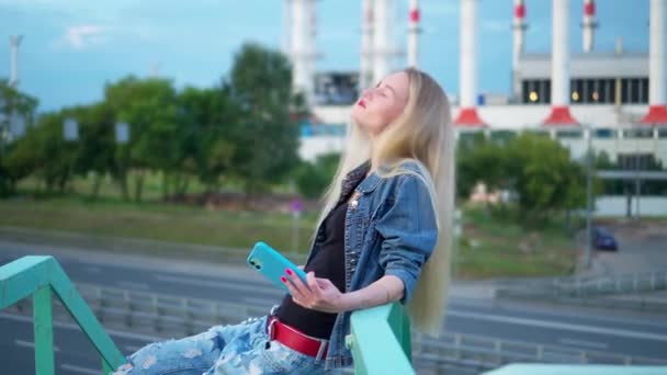 Una mujer joven, rubia, en las vías del tren, se toma un selfie en un smartphone. — Vídeos de Stock