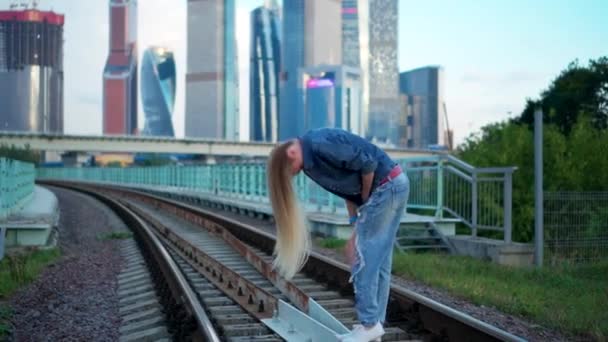 Tânără blondă merge pe calea ferată în oraș — Videoclip de stoc