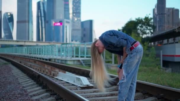 若いブロンドの女性が街の鉄道線路を歩く — ストック動画