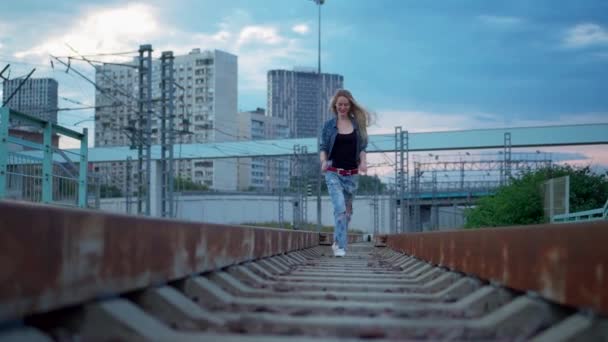 若いブロンドの女性が街の鉄道線路を歩く — ストック動画