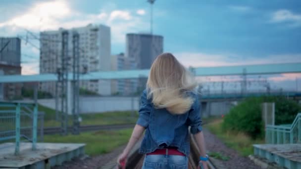 Молода блондинка ходить по залізничних коліях міста. — стокове відео