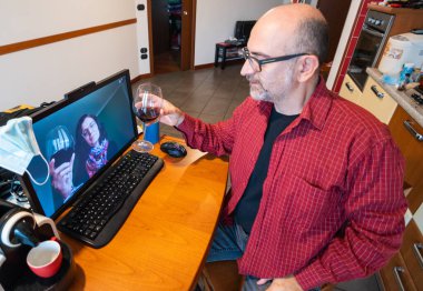 Coronavirus salgını, sosyal mesafeler selamlaşma anlamına gelir ve internette kadeh kaldırılır. Bir kadın uzaktan bağlanır ve adamı selamlar, kadehlerini kadeh kaldırmak için kaldırırlar..