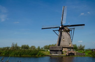 Kinderdijk, Hollanda, Ağustos 2019. Güzel bir yaz gününde, Hollanda kırsalında, uzun yeşil otlarla kaplanmış, mükemmel durumda, tarihi bir rüzgar değirmeni..