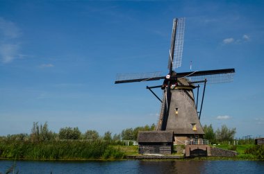 Kinderdijk, Hollanda, Ağustos 2019. Güzel bir yaz gününde, Hollanda kırsalında, uzun yeşil otlarla kaplanmış, mükemmel durumda, tarihi bir rüzgar değirmeni..