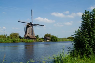 Kinderdijk, Hollanda, Ağustos 2019. Güzel bir yaz gününde, Hollanda kırsalında, uzun yeşil otlarla kaplanmış, mükemmel durumda, tarihi bir rüzgar değirmeni..