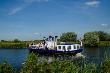 Kinderdijk, Hollanda, Ağustos 2019. Bir gezi teknesi, bölgenin tarihi yel değirmenlerini ziyaret etmek için Hollanda kırsal kesimindeki kanalları geziyor. Güneşli güzel bir gün, tekne kalabalık..