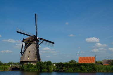 Kinderdijk, Hollanda, Ağustos 2019. Güzel bir yaz gününde, Hollanda kırsalında, uzun yeşil otlarla kaplanmış, mükemmel durumda, tarihi bir rüzgar değirmeni..