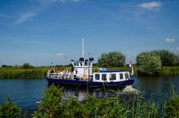 Kinderdijk, Hollanda, Ağustos 2019. Bir gezi teknesi, bölgenin tarihi yel değirmenlerini ziyaret etmek için Hollanda kırsal kesimindeki kanalları geziyor. Güneşli güzel bir gün, tekne kalabalık..